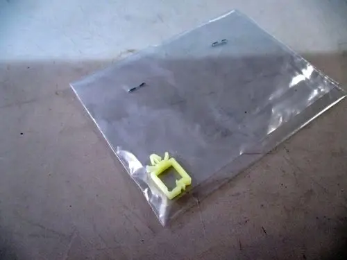 Transparente Plastiktüte mit einer gelben Halterung und zwei kleinen Metallklammern. Produkt von Wolf, möglicherweise Teil eines Kabelmanagementsystems.